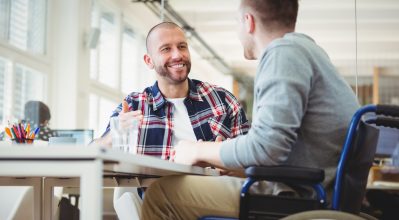 (alt="Colleagues chatting in an office, one of them is in a wheelchair")